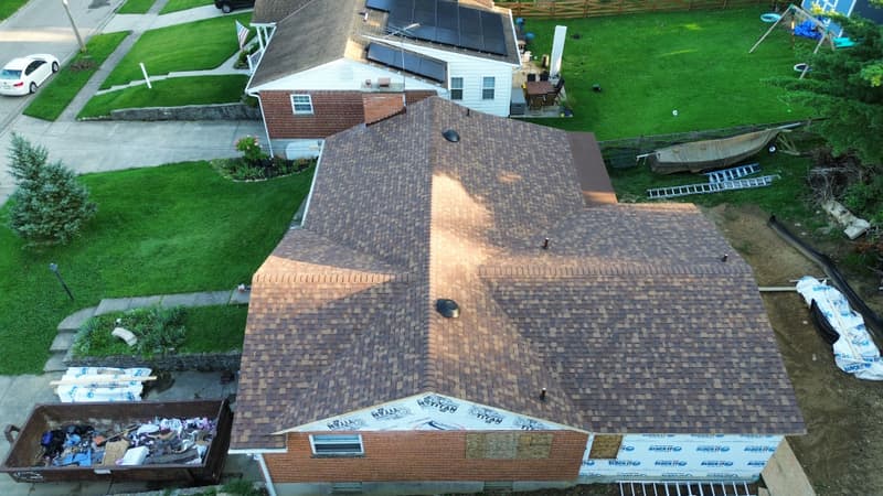 Aerial view of house with new shingles and debris dumpster